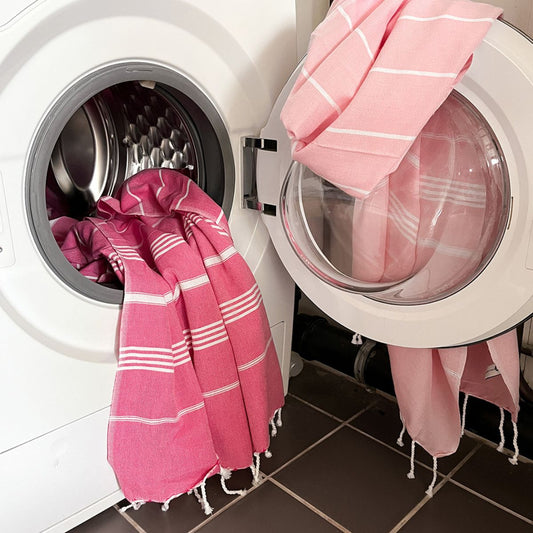Roze gestreepte hamamdoeken in een wasmachine als illustratie bij tips voor het wassen van een hamamdoek