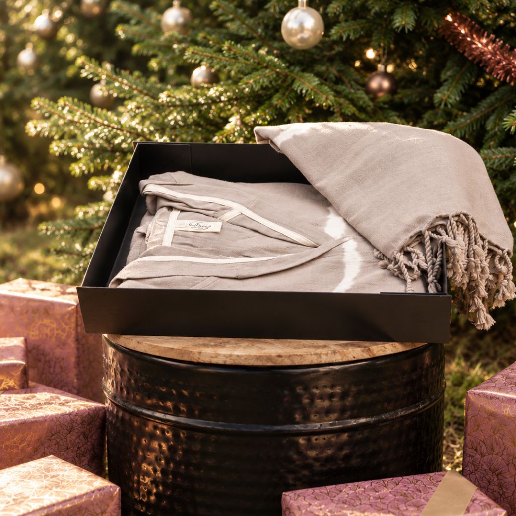 Luxe kerstcadeau met badjas en hamamdoek in zwarte cadeaudoos voor een versierde kerstboom