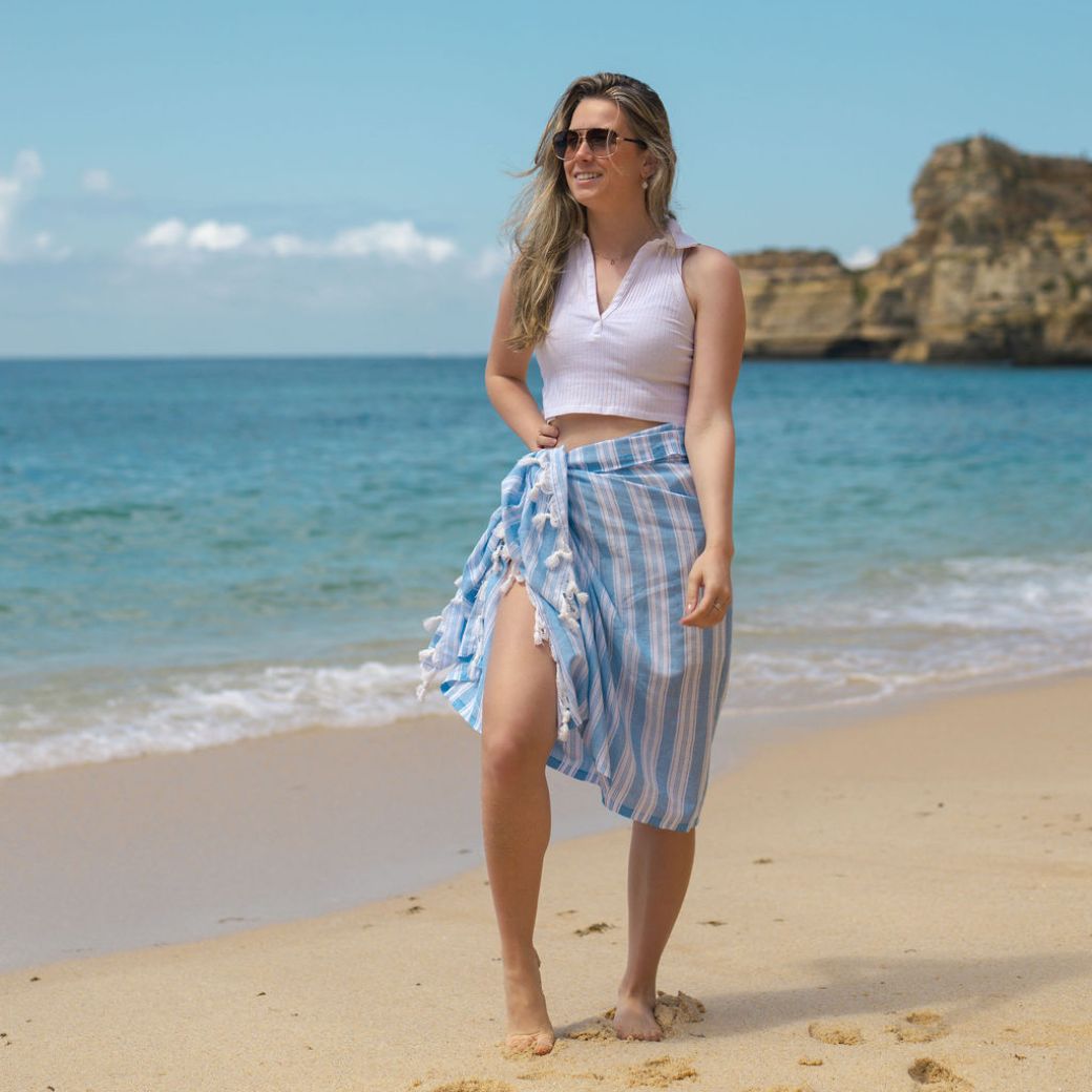 Vrouw draagt een blauw gestreepte pareo als omslagrok op het strand