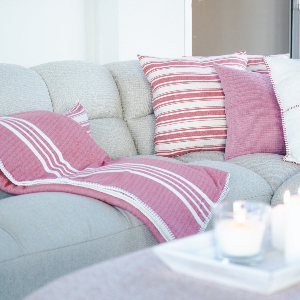 Roze plaid met witte strepen gedrapeerd over een lichte bank met bijpassende kussenhoezen.