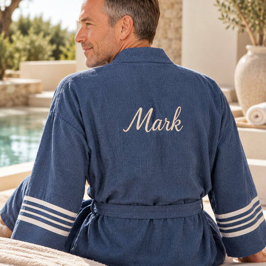 Man draagt blauwe hamam badjas met geborduurde naam Mark in een luxe wellnessomgeving.