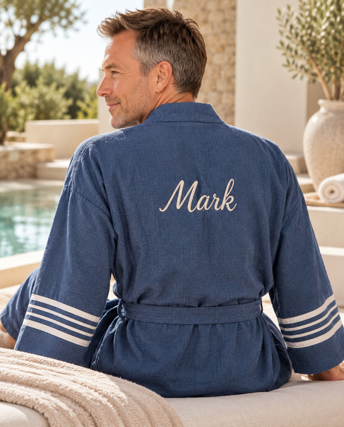 Man draagt blauwe hamam badjas met geborduurde naam Mark in een luxe wellnessomgeving.