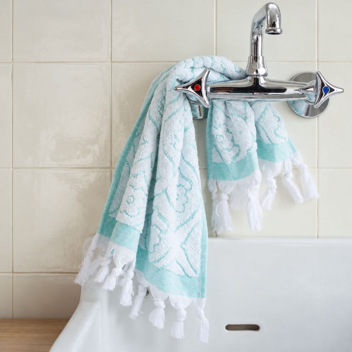 Mintgroene hamam handdoek met wit bloemenpatroon, badstofstructuur en geknoopte franjes, hangend over een chromen kraan in de badkamer.