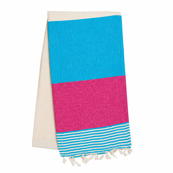 Opgevouwen hamamdoek in turquoise en fuchsiaroze, met naturel achterkant, turquoise-witte strepen en geknoopte franjes.