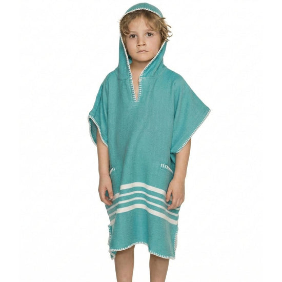 Kind draagt een turquoise strandponcho met capuchon, witte strepen en sierstiksels langs de randen.