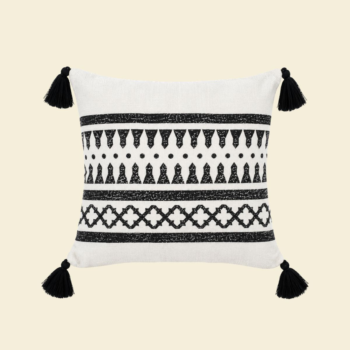 Witte kussenhoes met zwart etnisch patroon, geometrische motieven en zwarte tassels aan de vier hoeken met creme achtergrond.