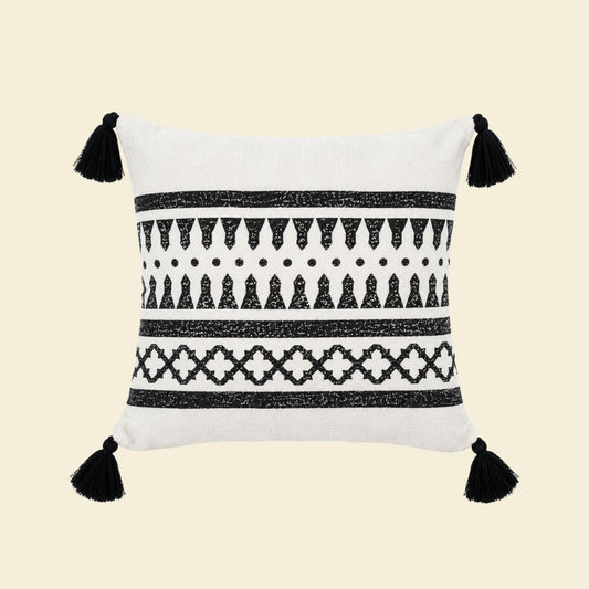 Witte kussenhoes met zwart etnisch patroon, geometrische motieven en zwarte tassels aan de vier hoeken met creme achtergrond.