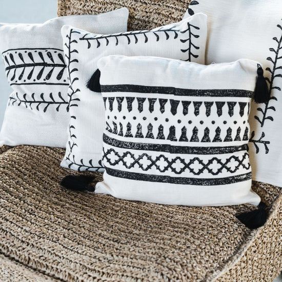 Zwart-witte kussenhoezen met geometrische patronen en zwarte tassels op een gevlochten stoel in boho stijl.