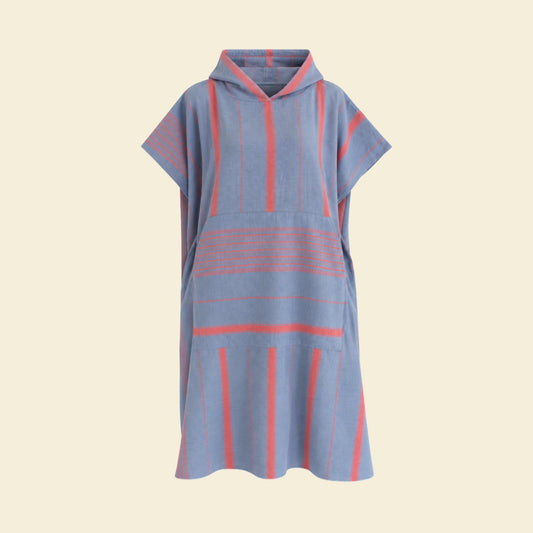 Staalblauwe Ottomania Ege surfponcho met steenrode strepen, capuchon en buidelzak op een crème achtergrond.