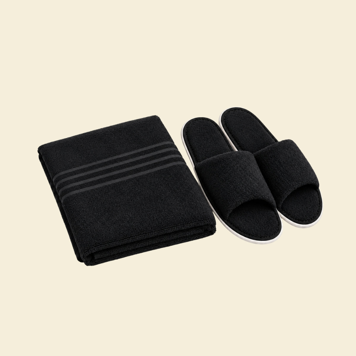 Zwart saunapakket met compact opgevouwen saunadoek en zwarte saunaslippers op crème achtergrond